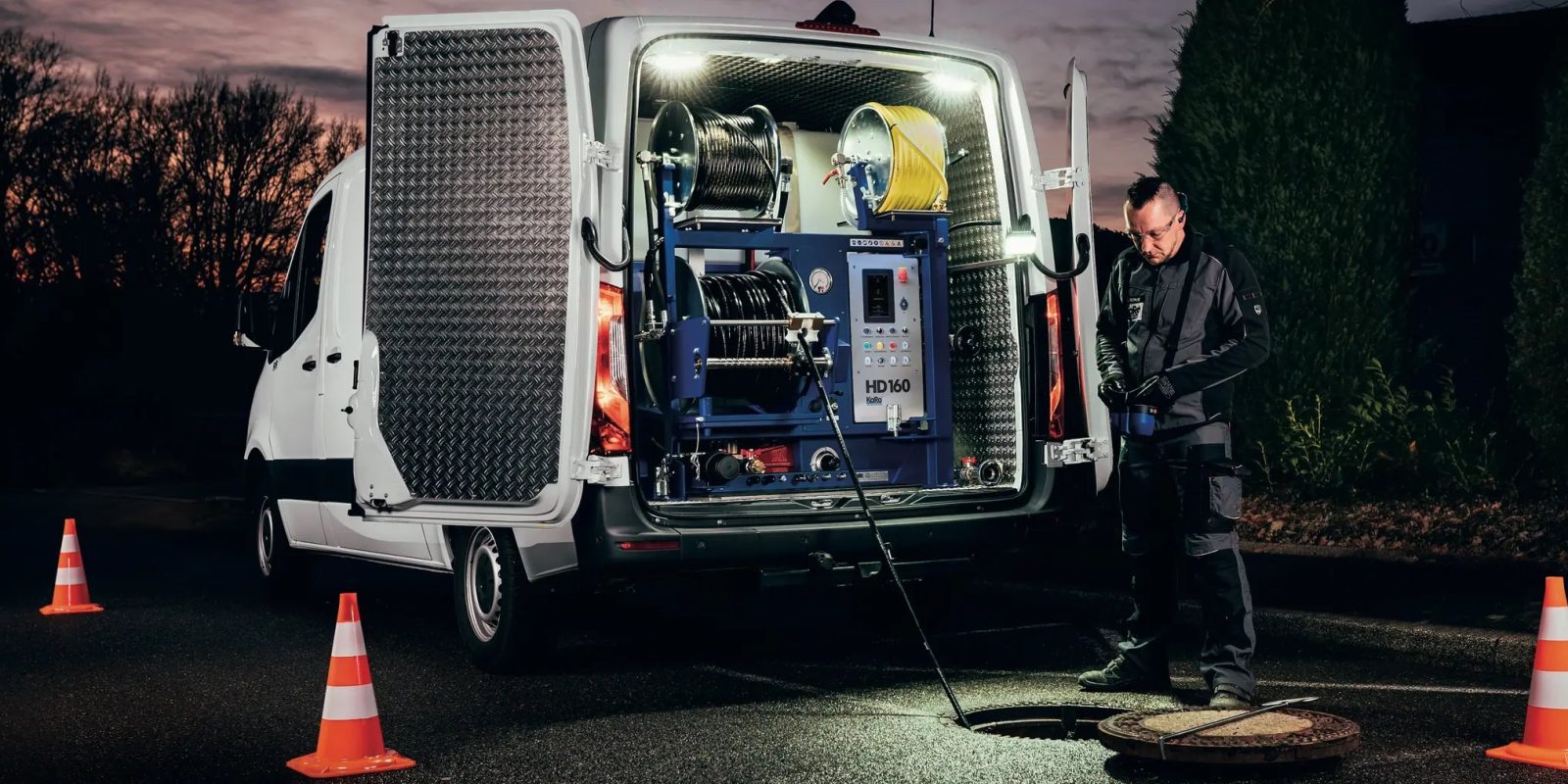 Transporter mit KaRo HD 160 Hochdruckeinbau in der Abenddämmerung, ein Techniker führt den Spülschlauch in einen offenen Kanalschacht