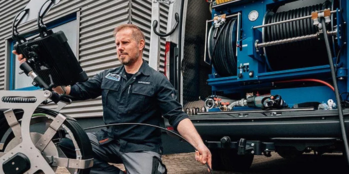 Techniker mit dem Steuergerät einer Kanalkamera vor einem Transporter mit blauem Hochdruckeinbau und zwei Schlauchhaspeln